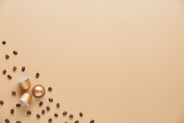 Caffeine, hot drinks and objects concept - close up of golden capsules or pods for coffee mashine with some roasted grains on beige background. Top view with space for text. Flat lay..