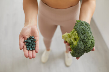 Woman holding fresh broccoli head and spirulina pills before making healthy smoothie