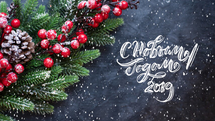 Happy New Year text in russian, hand lettering inscription with red balls, tree branches and cones on a dark background. Christmas greeting card.