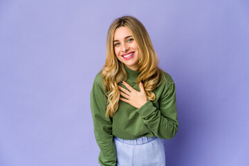 Young caucasian blonde woman laughs out loudly keeping hand on chest.