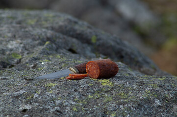 Knife cutting sausage in the mountain with blurry mountain landscape in background.  Outdoor food.