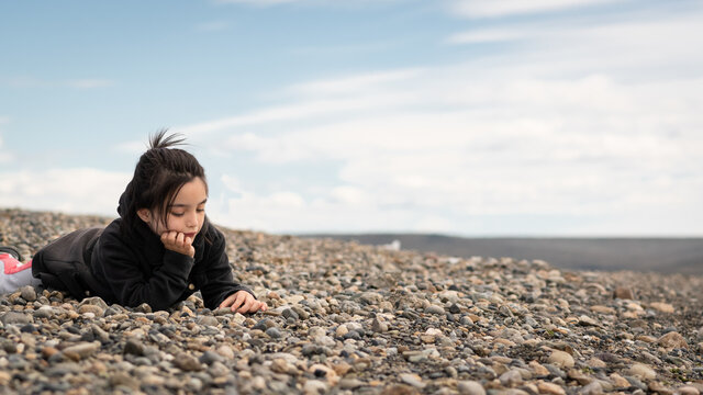 pequeña niña sentada en piedras con abrigo y pelo recogido
