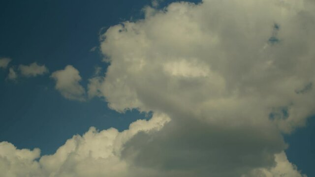 Thick white clouds float across the blue summer sky. Timelapse. Sunny.