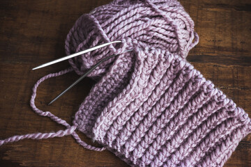 Knitting at home as a hobby. A skein of pale lilac woolen thread lies on a wooden table.
