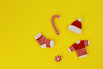 Fototapeta na wymiar decorative knitted ornaments sock, sweater, hat and caramel in red and white color on yellow background