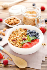 Tasty granola with fresh berries and spoon on brown wooden background