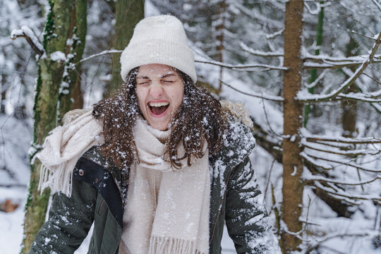 Young laughing funny happy girl, woman ,covered by snow walks in beautiful winter forest among trees, firs. Magnificent nature and views. Fashionable image, clothes, parka, hat, mittens, blue jeans