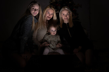 Little girl with her mother and aunts sitting in the dark  behind  magic box and posing  for a...
