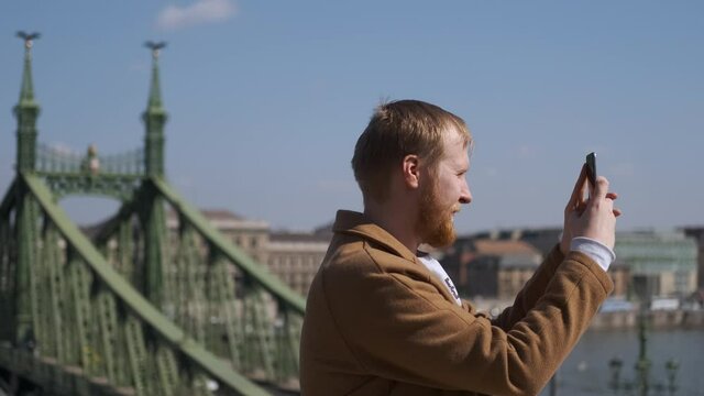 Caucasian man taking pictures on phone view of Liberty Bridge
