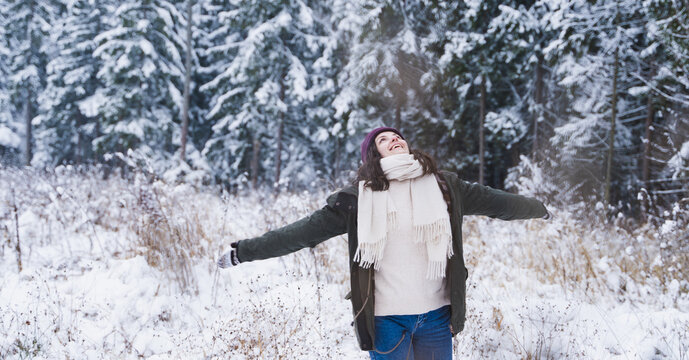 Young girl, woman walks in beautiful winter forest among trees, firs, covered with snow. Magnificent nature and views. Fashionable image, clothes, parka, hat, mittens, blue jeans
