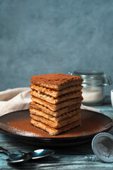 A stack of cocoa-dusted waffles on a wooden gray-blue background. Side view. The concept of cooking.