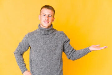 Young caucasian handsome man showing a copy space on a palm and holding another hand on waist.