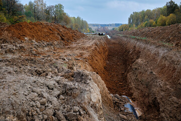 A dug trench, a pit for laying large-diameter pipes against the backdrop of an autumn forest. Construction of a gas pipeline or oil pipeline.