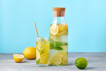 Fresh homemade lemonade with lime and mint in the glass with paper straw and bottle on bright blue background