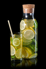 Fresh homemade lemonade with lime, mint and ice in the bottle and glass with paper straw isolated on black background