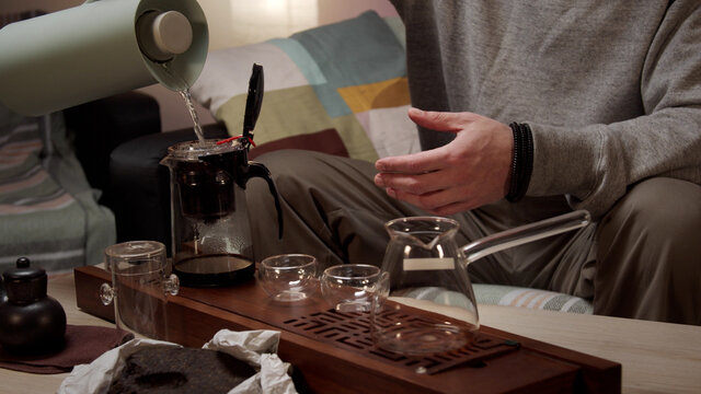 Unrecognizable man pours boiling water from a thermos into a teapot with tea leaves, brews tea during a tea ceremony