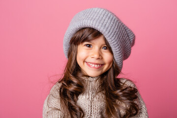 little brunette girl with long hair in winter clothes on a pink background in the Studio. knitwear for children, space for text