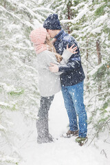 passionate couple kissing in winter forest under snowfall