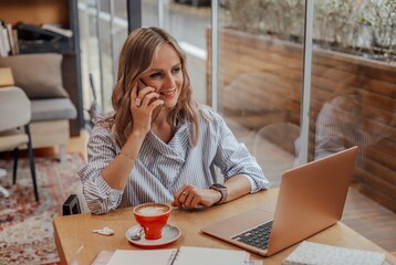 A smiling young woman sits in a cafe and talks on the phone.