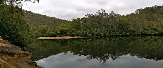 Beautiful view of a creek with reflections of cloudy sky, mountains and trees on water, Crosslands Reserve, Berowra Valley National Park, New South Wales, Australia
