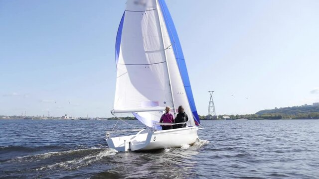 River trip of three friends on a clear day on a yacht with a white and blue sail. Fast dynamic shot with slow motion.