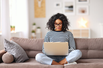 Smart ethnic woman using laptop on sofa.