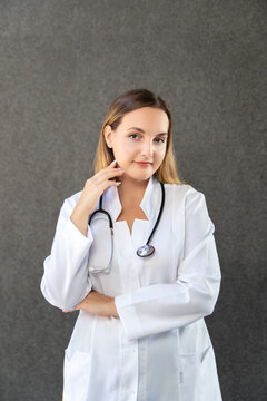 Portrait of a modern doctor's girl standing isolated on a gray background with a stethoscope, holding her hand to her face. Studio, copy space. Medicine, healthcare and profession concept.