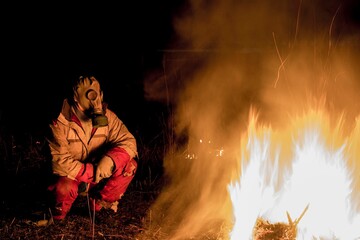 Obraz premium a man in a gas mask in a poor environment after a pandemic at night near the fire