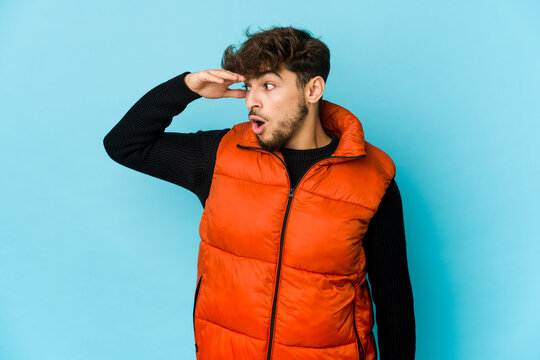 Young Arab Man On Blue Background Looking Far Away Keeping Hand On Forehead.