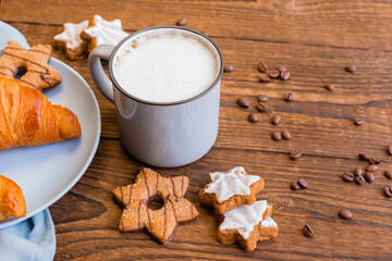 A mug of coffee with milk and foam, latte, cappuccino on a wooden table next to a fresh croissant and New Year's garlands. Festive, Christmas coffee