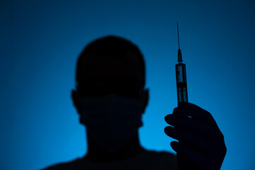 A doctor in a medical mask and gloves holds a syringe with a coronavirus vaccine and a vaccine chip...