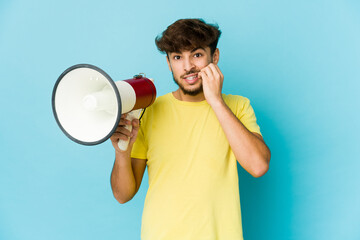 Young arab man holding a megaphone biting fingernails, nervous and very anxious.