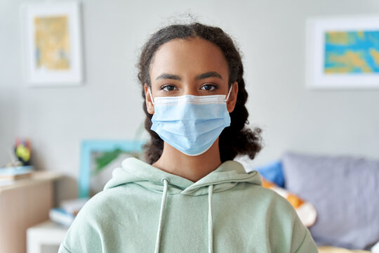 African American Teen Girl Wearing Face Mask Looking At Camera At Home. Mixed Race Teenager During Pandemic Quarantine Concept. Children Safety For Covid Protection, Close Up Headshot Portrait.