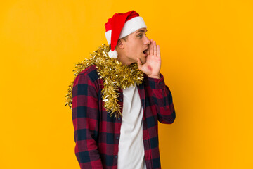 Young caucasian man with christmas hat holding a present isolated on yellow background