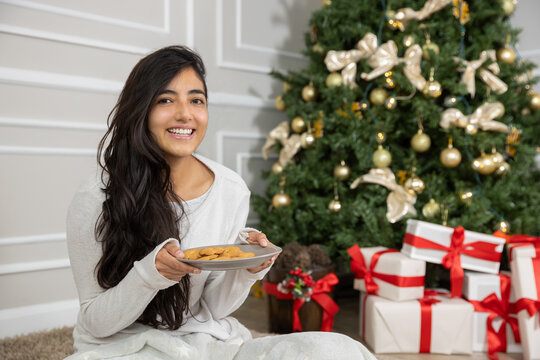 Mexican Latin Woman Holding A Plate With Cookies In Front Of A Christmas Tree