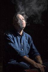 Matured bald man smoking, portrait on black background.