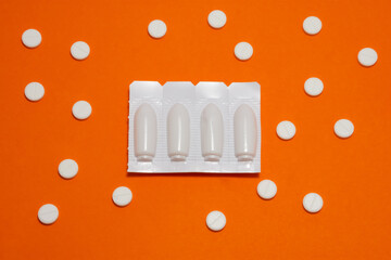 A medicinal product or drugs  in  form of vaginal or rectal medical suppositories in white package lies on a red background, which symbolizes the pain from hemorrhoids or thrush, surrounded by pills