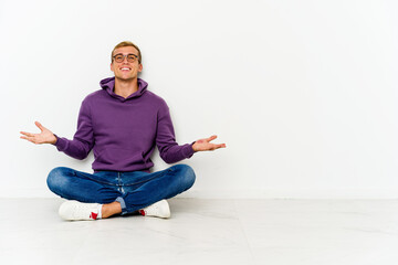 Young caucasian man sitting on the floor showing a welcome expression.