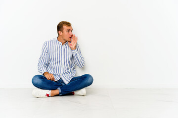 Young caucasian man sitting on the floor is saying a secret hot braking news and looking aside