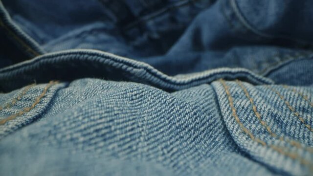 Macro shot of blue denim jeans material. Slider dolly extreme close-up of clothing material fabric texture. Seams sewn with yellow threads. Shot with laowa 24mm lens
