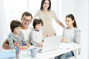 Happy latin family with children spending time together at home. Father watching kids playing, drawing while working from home, using laptop