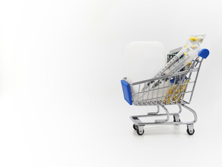 The second, the third wave of coronavirus. Mini shopping cart with medicine from Covid-19. Vaccine, syringes and pills on a light background.