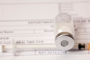Vaccine vial, syringe, on top of PCR medical form for covid-19