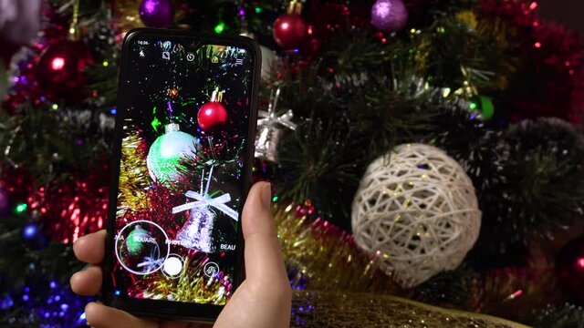 Photo of a Christmas tree for social networks.4kA female hand makes a photo of a Christmas elegant tree using a smartphone.