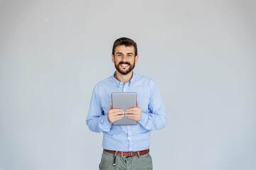 Smiling bearded businessman standing in front of white wall and holding tablet. Technology is important if you want your business on higher level.