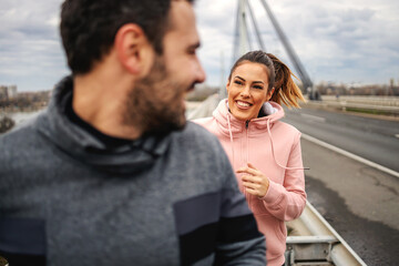 Smiling happy sporty couple running on the bridge at autumn at cloudy weather and preparing for...