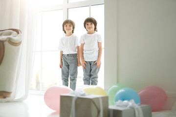 Fototapeta premium Lovely twins. Two cute latin twin boys, little children in casual wear looking happy, greeting their parents, preparing colorful balloons and giftboxes for them