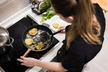 Young charming Swedish woman cooking at home in her kitchen, preparing healthy mediterranean food for her family. Young food blogger doing food preparation in her kitchen, frying vegetables