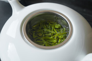 Ding Gu Da Fang, fresh green tea leaves, spring harvest. From Anhui mountain in China. Processed similarly to the famous Long Jing Dragon Well. Leaves is steeping in a porcelain teapot.