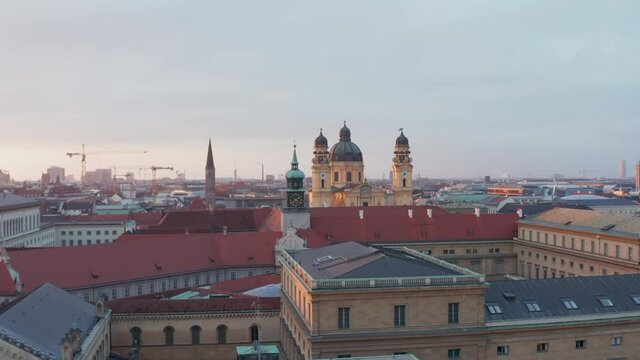 Theatine Church, Munich, Yellow Cathedral in beautiful Sunset Golden Hour light, big German City on beautiful Winter Day with clear sky, Aerial Dolly in flight above Red rooftops